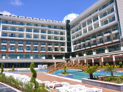 Großes Hotel mit Pool, Liegestühlen und grüner Bepflanzung unter blauem Himmel.