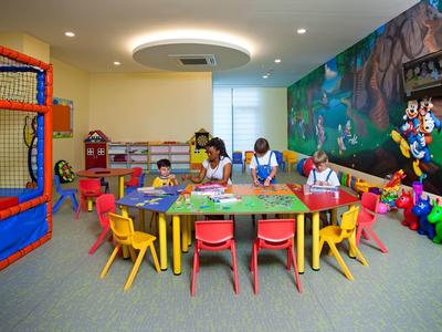 Kinderspielzimmer mit bunten Tischen, Stühlen, Klettergerüst und Wandmalerei.
