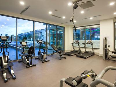 Moderner Fitnessraum mit Laufbändern, Fahrrädern und großem Panoramafenster zur Außenansicht.