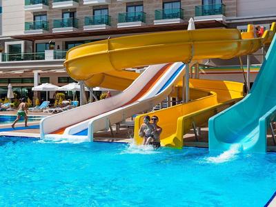Mehrere bunte Wasserrutschen führen in ein klares Schwimmbecken im Außenbereich eines Hotels.
