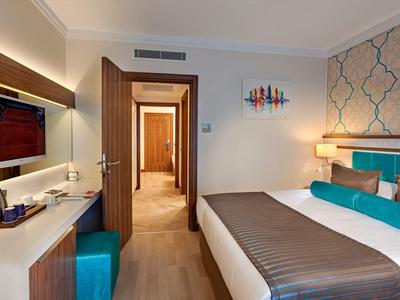 Modern eingerichtetes Hotelzimmer mit Doppelbett, blauen Akzenten und Flur mit offenem Türrahmen.