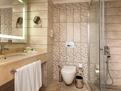 Modernes Badezimmer mit weißer Toilette, beleuchtetem Spiegel und Dusche mit Glasabtrennung.