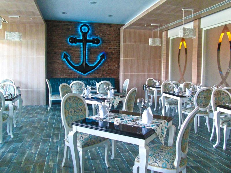 Restaurante elegante con sillas blancas y ancla azul en la pared de fondo.