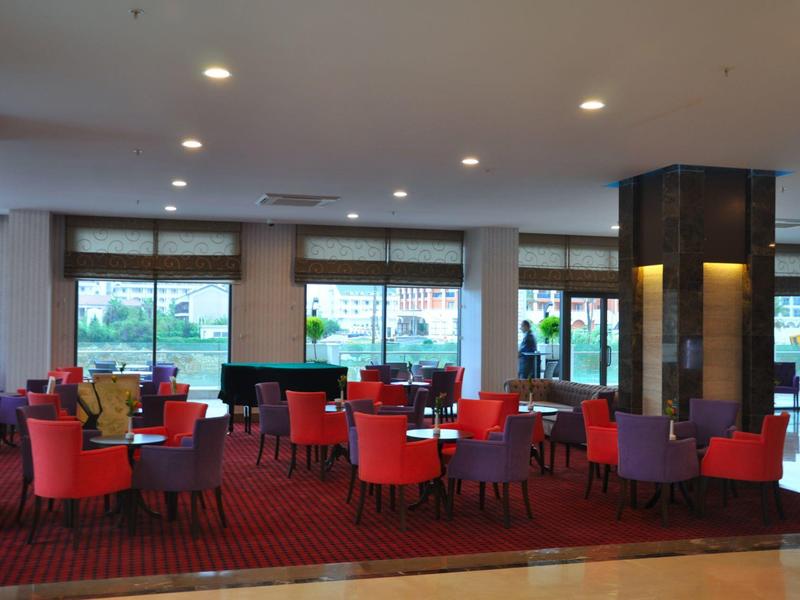 Restaurante de hotel iluminado con sillas coloridas, mesas, grandes ventanales y alfombra.