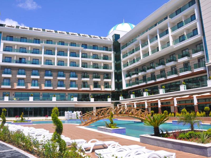 Complejo hotelero moderno con piscina al aire libre, tumbonas y jardín cuidado bajo sol.