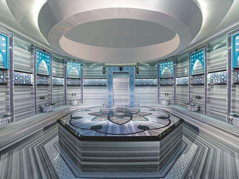 Hamam moderno con paredes de mármol, piscina central y luces de techo redondas.