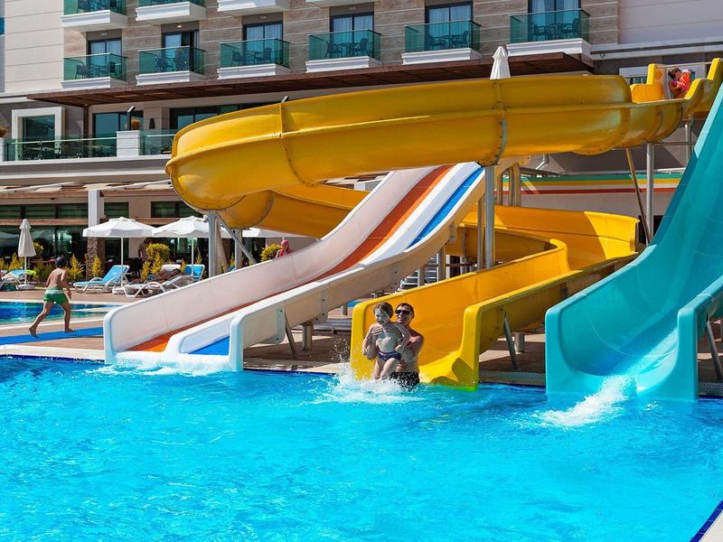 Varias toboganes de agua de colores desembocan en una piscina azul de hotel bajo el sol.