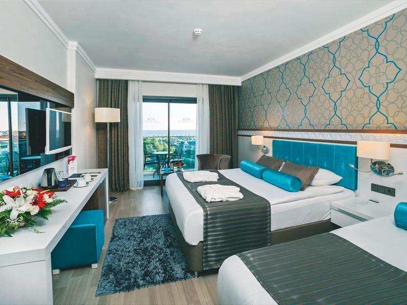 Habitación de hotel con dos camas, decoración azul y blanca y acceso a un balcón con vista verde.