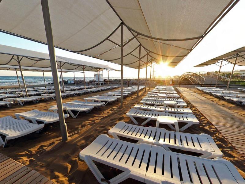 Sillas reclinables vacías bajo protección solar en la playa al atardecer con vista al mar.