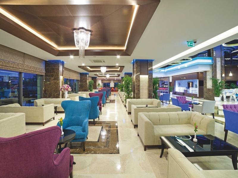 Sala moderna de hotel con sillones coloridos, sofás y elegante iluminación en el techo al anochecer.