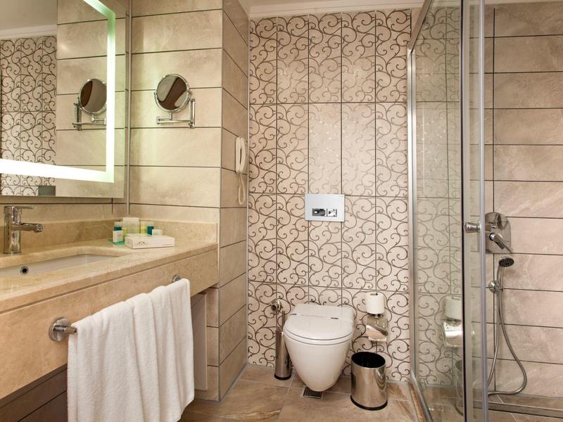 Baño moderno con paredes de azulejos, espejo iluminado e inodoro en una habitación de hotel.