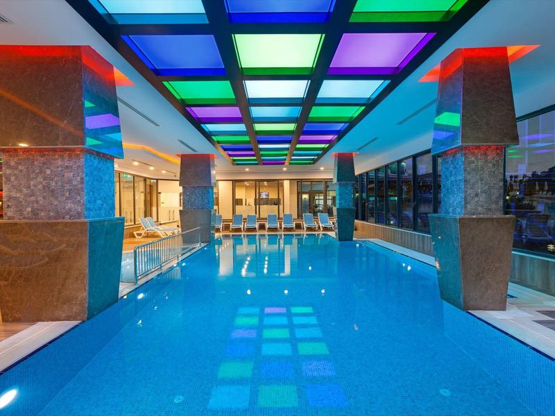 Piscina interior con luces de techo coloridas y columnas modernas en un hotel.