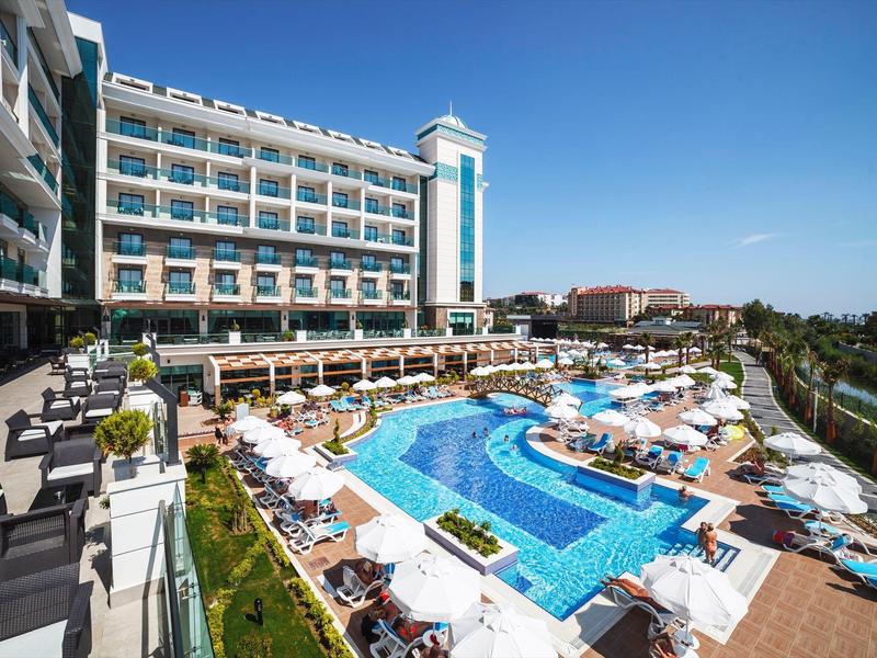 Gran hotel con terraza, piscina y tumbonas bajo un cielo despejado.
