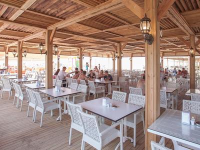 Large outdoor dining area with wooden roof and white chairs by the sea.