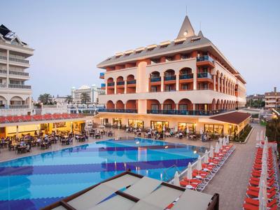 Hôtel avec grande piscine extérieure, transats et clients au coucher du soleil.