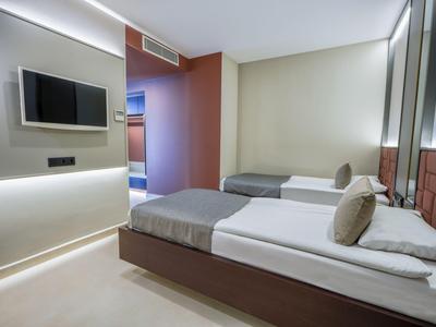 Chambre d'hôtel moderne avec deux lits simples, TV murale et design minimaliste.