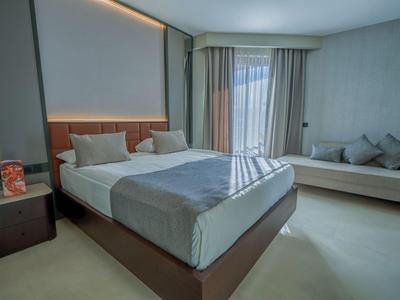 Chambre d'hôtel moderne avec lit double, canapé et fenêtre avec rideaux.