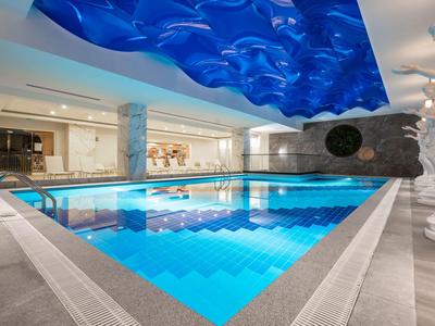 Kryty basen z niebieską wodą, nowoczesnymi kolumnami i falistym sufitem w hotelu.