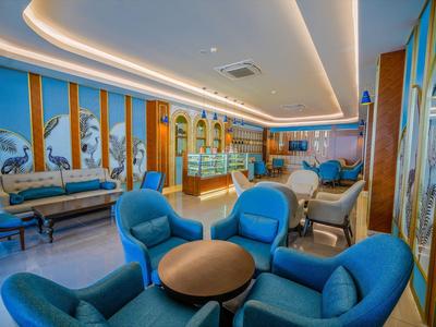 Nowoczesny salon hotelowy z niebieskimi fotelami, drewnianymi stolikami i oświetleniem pośrednim.
