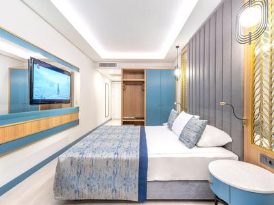 Nowoczesny pokój hotelowy z podwójnym łóżkiem, niebieskimi panelami ściennymi i telewizorem na ścianie.