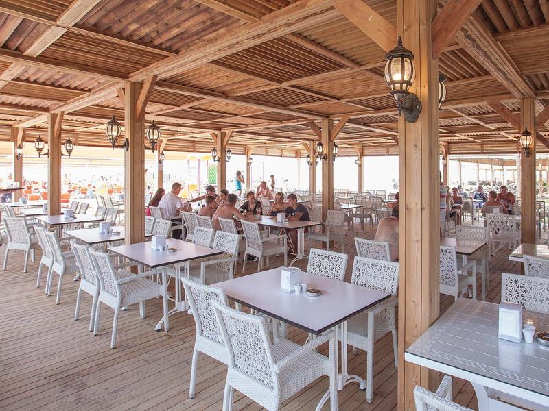 Large outdoor dining area with wooden roof and white chairs by the sea.