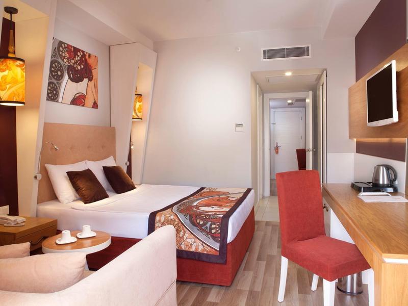 Modern hotel room with double bed, desk, TV, and stylish warm-colored accents.