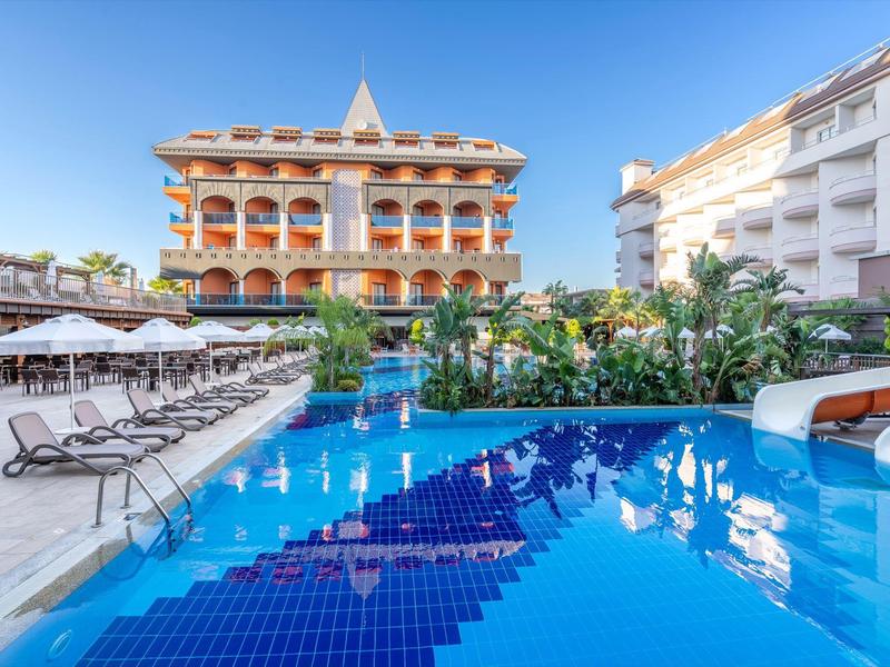 A hotel with a large blue pool and sun loungers under white umbrellas.