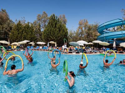 Menschen im Schwimmbecken üben mit bunten Hula-Hoop-Reifen, umgeben von Bäumen und blauen Wasserrutschen.