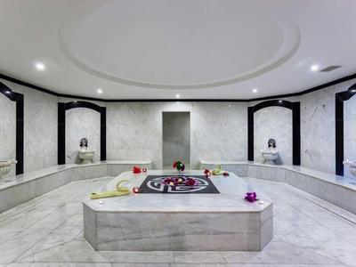 Weißer, moderner Hammam mit zentralem Wasserbecken und umliegenden Marmorliegen in symmetrischem Design.