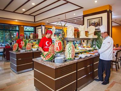 Buffet mit bunt dekoriertem Obst und Gemüse, zwei Köche in Rot und Weiß, helles Restaurant.