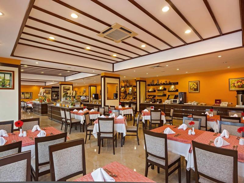 Nowoczesna jadalnia z pomarańczowymi ścianami, przygotowanymi stolikami i tapicerowanymi krzesłami.