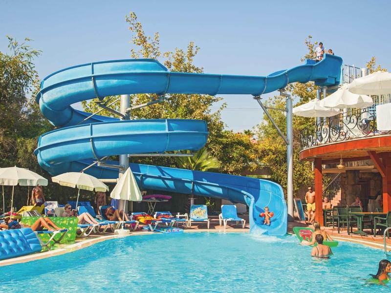 Duży basen z niebieską zjeżdżalnią i leżakami pod parasolami.
