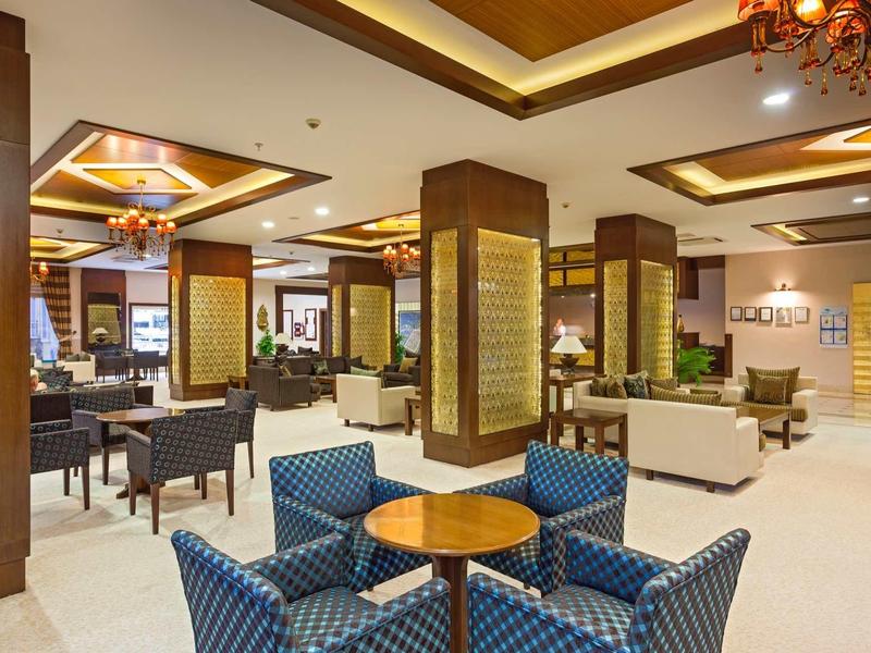 Elegancki hol hotelowy z niebieskimi fotelami, drewnianymi stolikami i nowoczesnym oświetleniem.