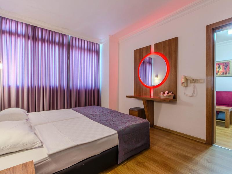 Przytulny pokój hotelowy z podwójnym łóżkiem, fioletowymi zasłonami i drewnianą podłogą.