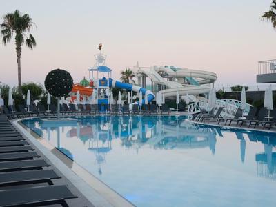 Groot zwembad met glijbanen en ligstoelen bij zonsondergang.