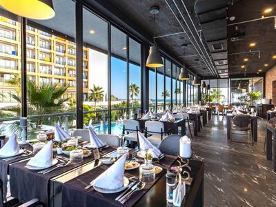 Modern restaurant met grote ramen en stijlvol gedekte tafels naast een hotel.