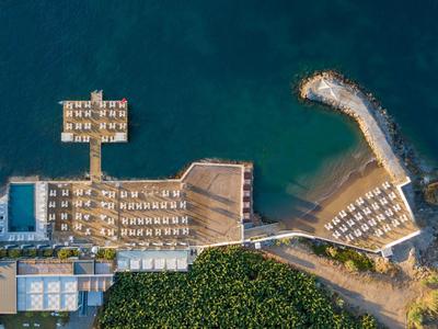Luchtfoto van een strand met ligstoelen, zwembaden en een bosrijk gebied ernaast.