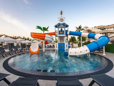 Rond zwembad met kleurrijke glijbanen en ligstoelen bij zonsondergang.