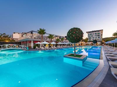 Piscina moderna dell'hotel con sdraio, palme e piante decorative al tramonto.