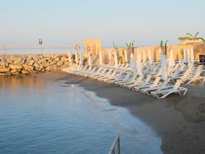Lege ligstoelen en parasols op het rustige strand met een rotsachtige golfbreker op de achtergrond.