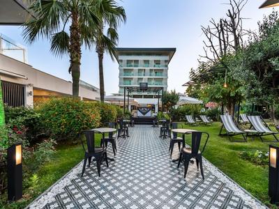 Jardin d'hôtel moderne avec chemin pavé, chaises, transats et palmiers en plein jour.