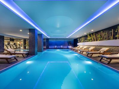 Espace piscine intérieure moderne avec éclairage bleu et chaises longues dans un hôtel.