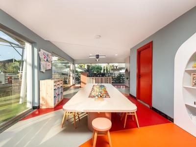 Salle à manger moderne avec une grande table, des tabourets et de grandes fenêtres donnant sur l'extérieur.