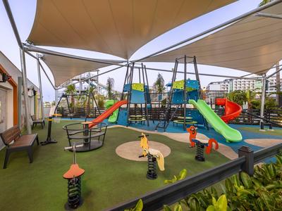 Aire de jeux moderne pour enfants avec toboggans et structures d'escalade dans un espace extérieur d'hôtel.