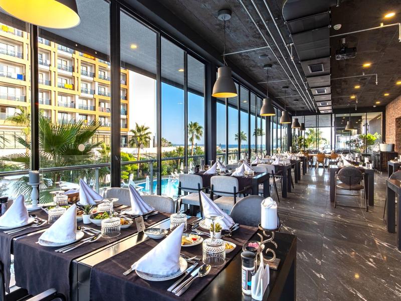 Modern restaurant met grote ramen en stijlvol gedekte tafels naast een hotel.