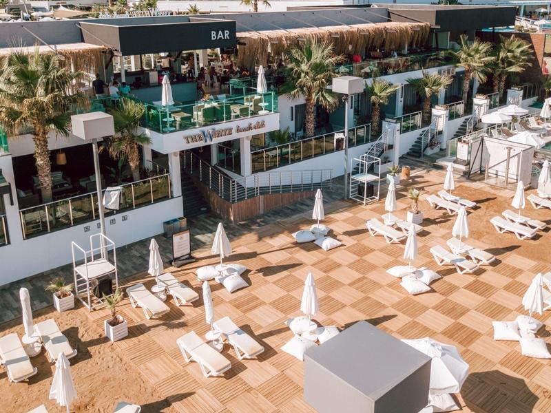 Moderne buitenruimte van een hotel met ligstoelen, parasols en palmbomen.