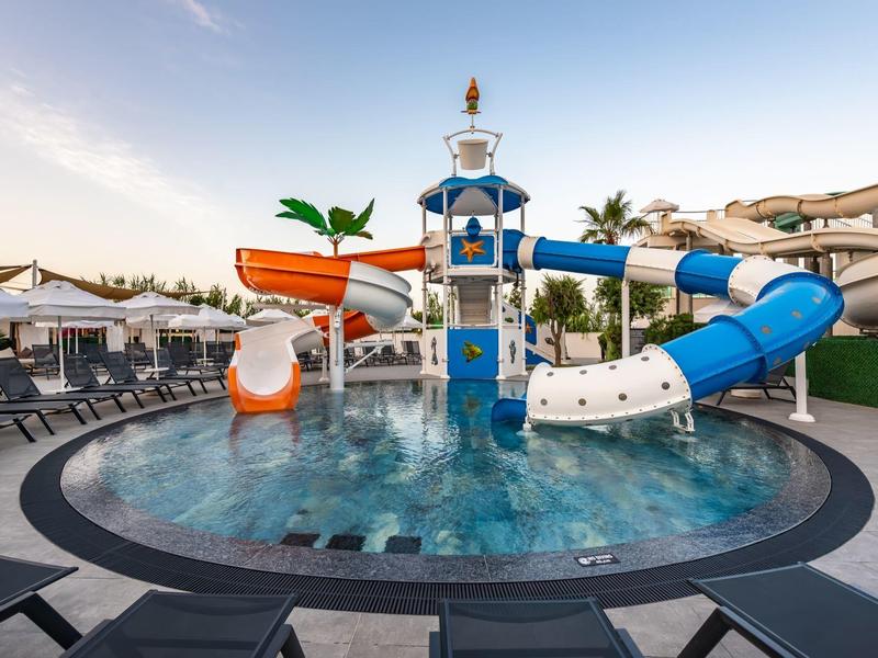 Rond zwembad met kleurrijke glijbanen en ligstoelen bij zonsondergang.