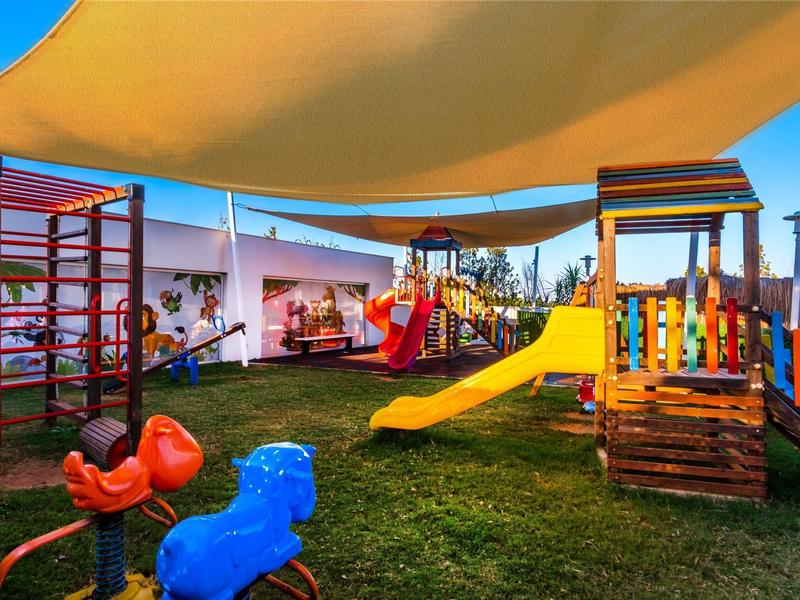 Kleurrijke buitenspeelplaats voor kinderen met glijbaan en klimrek onder zonneschermen.