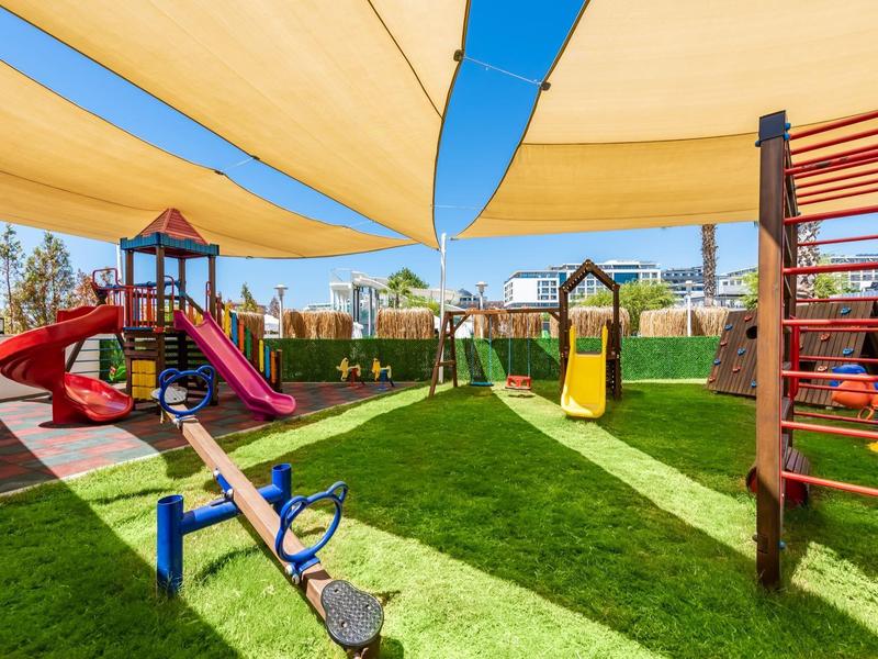 Goed onderhouden speeltuin met glijbanen, wip en klimrekken onder kleurrijke zonneschermen.