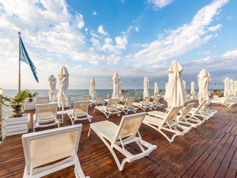 Ligstoelen en parasols op een houten terras met uitzicht op zee onder een bewolkte lucht.